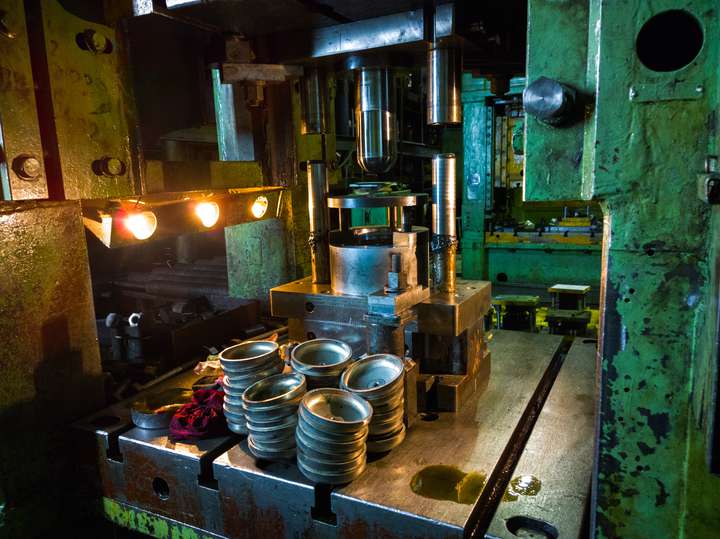Deep drawing process in a dark and dirty environment with finished products on the foreground of the press